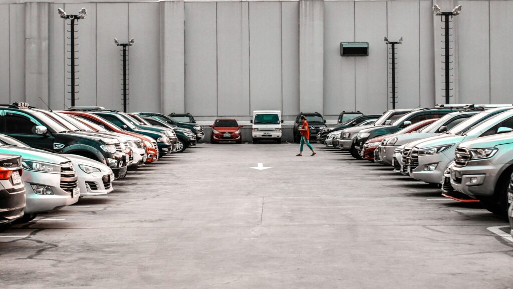 A sleek gray sedan displayed in a bright, modern showroom with large windows, and customer checking cars “New Tariffs, New Prices: Is Buying a Car Now a Financial Win or a Costly Mistake?