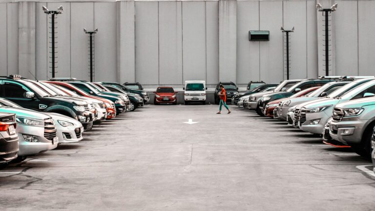 A sleek gray sedan displayed in a bright, modern showroom with large windows, and customer checking cars “New Tariffs, New Prices: Is Buying a Car Now a Financial Win or a Costly Mistake?